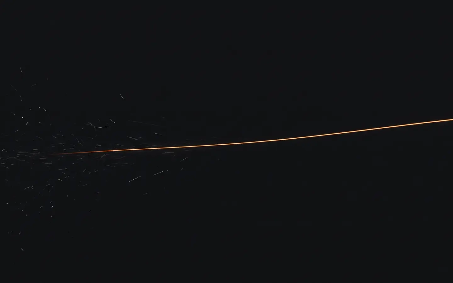 A single clean line of amber light crossing a dark field while faint sparks fade out on the left